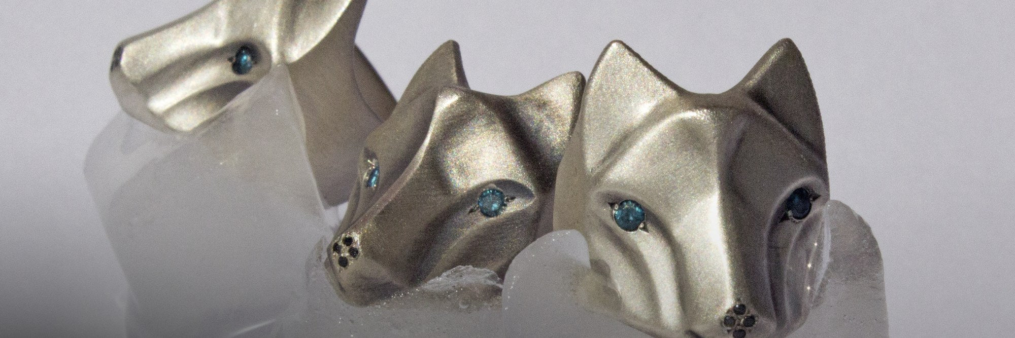 Three handmade sterling silver wolf rings with blue diamond eyes resting on ice
